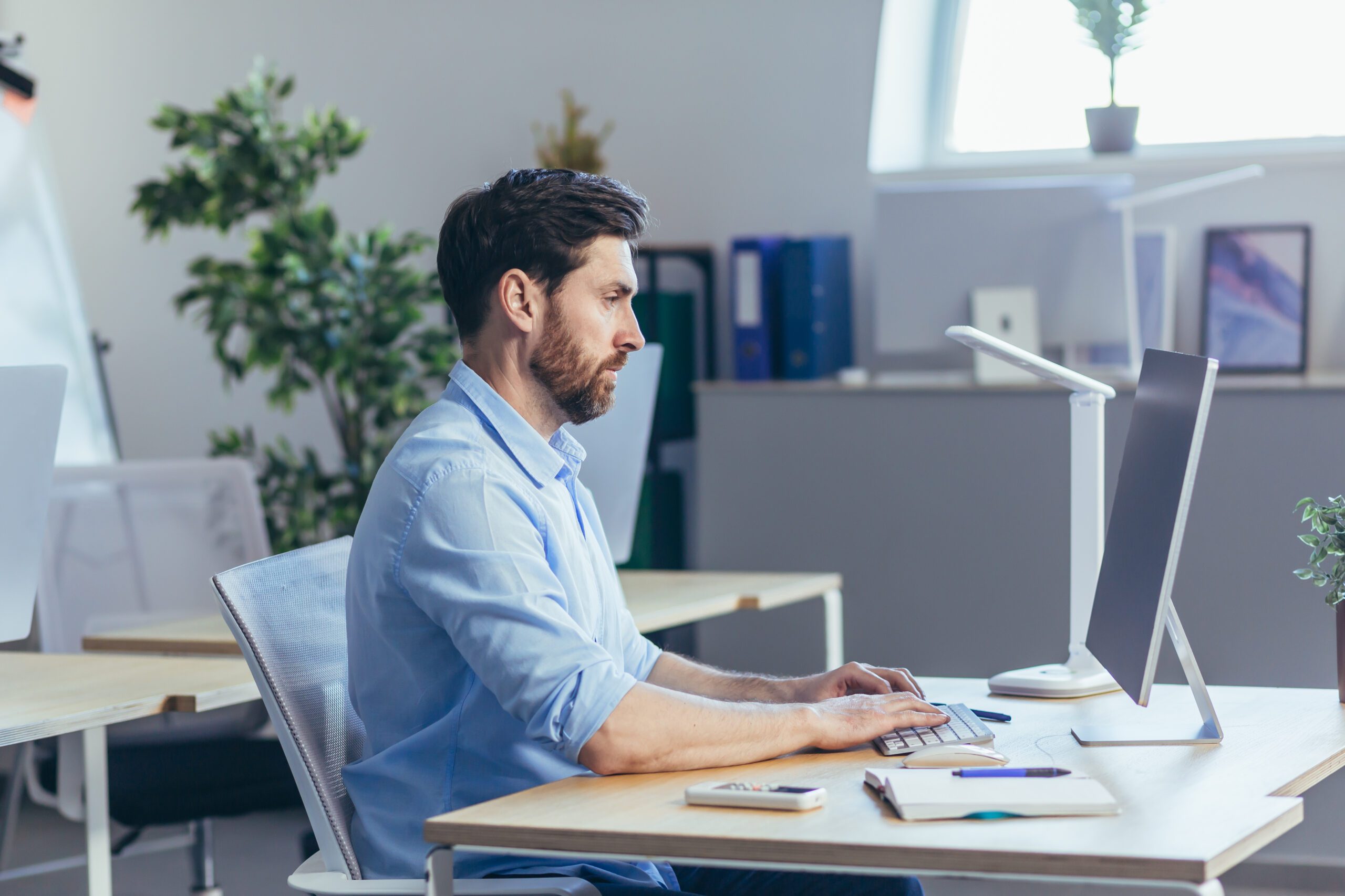 Portrait of a serious and focused businessman, a man working in a bright office during the day, at the computer looking at the monitor, in casual clothes